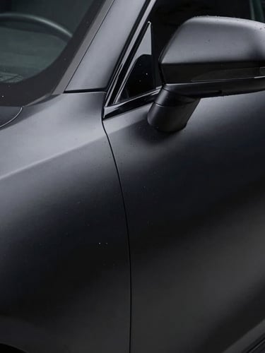 Extreme close-up of a perfectly applied matte black liquid wrap finish on a car panel, studio lighting, showing texture and precise edge-to-edge coverage, 50mm.