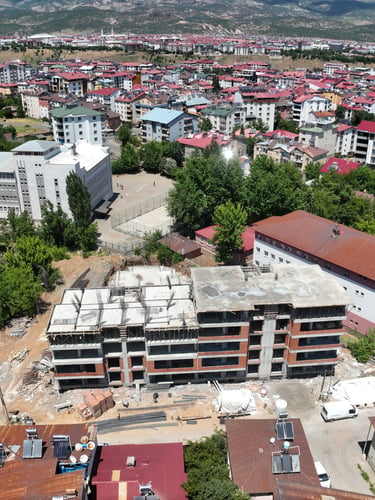 Aerial view of an apartment building under construction in a Turkish city with red-roofed houses.