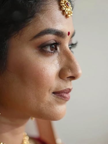Macro close-up of a South Asian bride's profile, soft diffused morning light catching luminous skin texture, delicate gold jewelry, clean negative space to the right.