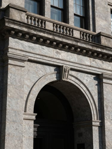 Dramatic architectural detail of a classic stone corporate entrance in Wilmington, Delaware, sharp directional daylight with high contrast, deep shadows.