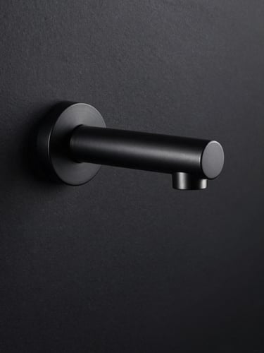 Tight vertical studio shot, a single matte black wall-mount faucet centered in frame against deep charcoal background, dramatic single-source side lighting from the left reveals brushed metal finish and precise machined edges, portrait orientation, no lifestyle context