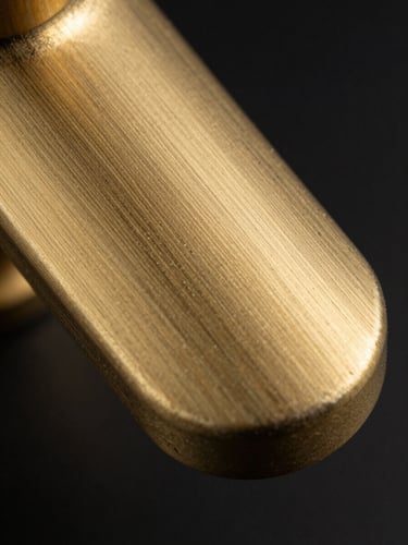 Extreme close-up macro of a brushed-gold faucet lever surface, strobe light raking across the metal at a low angle to reveal the fine parallel brushing texture and material depth, black background, no context, pure material study