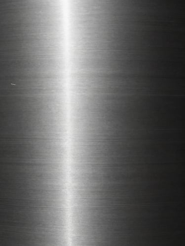 Extreme close-up of brushed steel texture with sharp linear reflections, high-contrast museum lighting, monochrome, 35mm