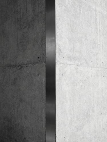 Minimalist architectural detail of a concrete corner meeting brushed steel under hard, high-contrast sunlight, sharp shadows, monochrome, 35mm