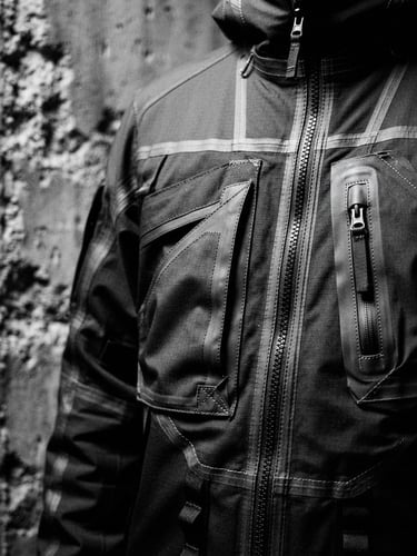 Close-up of a technical streetwear jacket with reinforced seams, high-contrast monochrome, brutalist concrete background, cold moon lighting, sharp focus, 35mm film grain