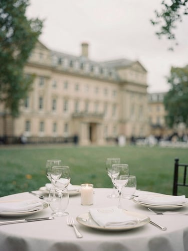 Elegant table setting with historic London architecture blurred in the background, soft overcast daylight, warm cream and forest green tones, 35mm photography