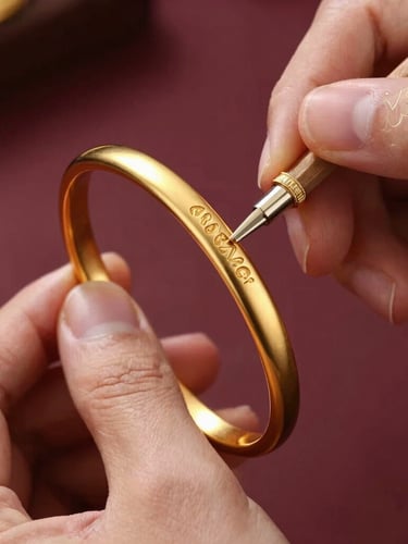 Extreme close-up of a master goldsmith's hands gently polishing a heavy gold bangle, warm directional spotlight catching the intricate metalwork and the tiny hallmark laser engraving, 35mm
