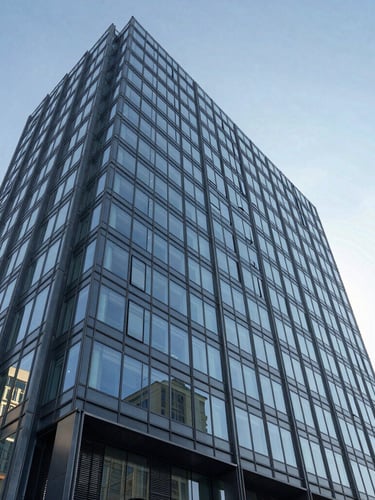 Vista en ángulo de la fachada de un moderno edificio corporativo de cristal y acero bajo una luz clara y fría, líneas arquitectónicas precisas.