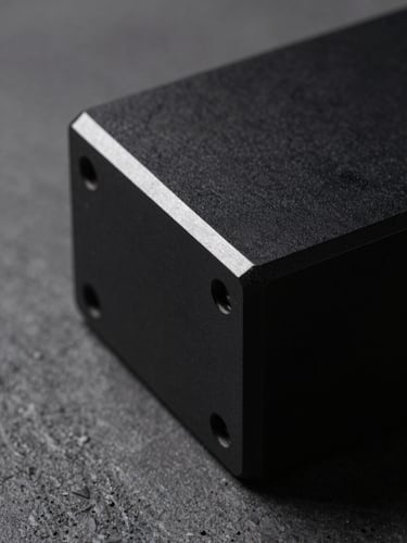 Macro studio shot of a machined matte-black aluminum device edge, sharp dramatic highlight on the metallic bevel, dark concrete background