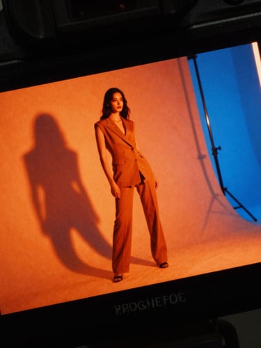 Close-up macro crop of a professional camera monitor displaying a high-contrast fashion shoot, vibrant orange neon edge-lights, sharp shadows, raw 35mm film grain.
