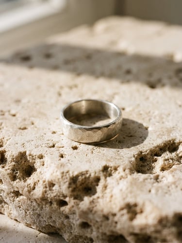 Close-up macro shot of an unpolished sterling silver ring resting on raw travertine stone, warm natural window light casting soft architectural shadows, 35mm film style
