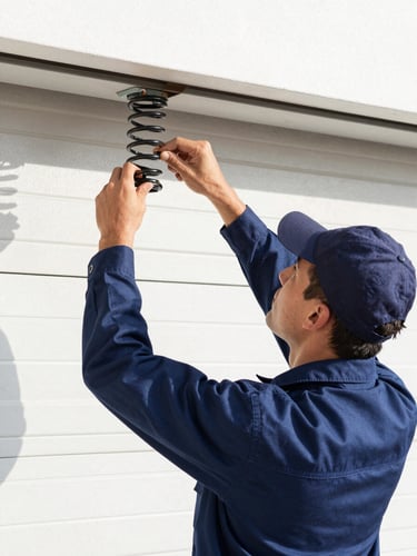 A clean commercial photograph of a professional technician in a dark blue uniform adjusting a garage door spring, bright natural daylight, high-contrast true colors, sharp focus, 35mm lens