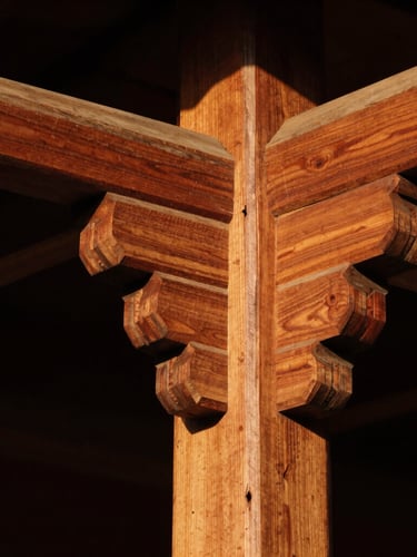 Extreme close-up of traditional Javanese wooden joinery, knock-down system, rich teak wood texture, dramatic golden-hour sunlight casting sharp shadows, high-contrast architectural photography