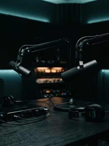 Cinematic low-key studio shot of a high-end podcast studio setup, professional microphones on boom arms, deep shadows with subtle teal rim lighting, shallow depth of field, 50mm lens