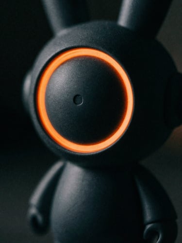 Macro shot of a custom vinyl art toy with sharp orange rim lights, dark dramatic photography, high-contrast chiaroscuro, deep charcoal tones, 35mm film grain