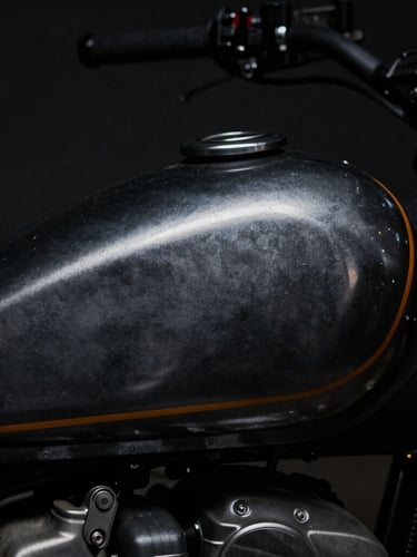 Macro close-up of custom-painted motorcycle tank with raw metal textures, dramatic low-key chiaroscuro lighting, deep charcoal tones