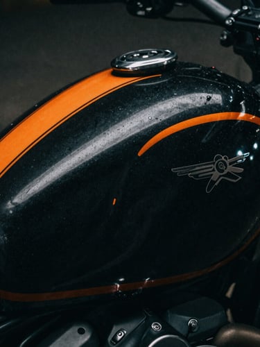 Extreme close-up of a custom-painted motorcycle tank with sharp orange pinstriping, dark dramatic photography, low-key chiaroscuro lighting, deep charcoal tones, 35mm film grain