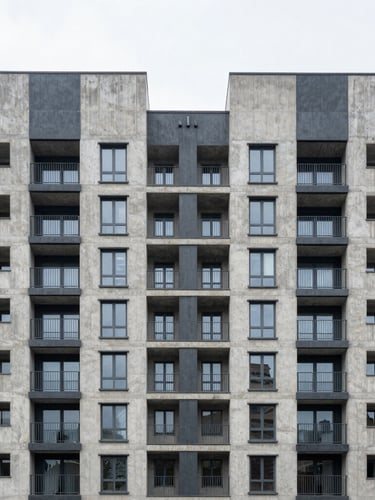 Straight-on symmetrical architectural facade of a modern concrete and steel residential building, stark gray tones, flat bright daylight, emphasis on spatial grid.