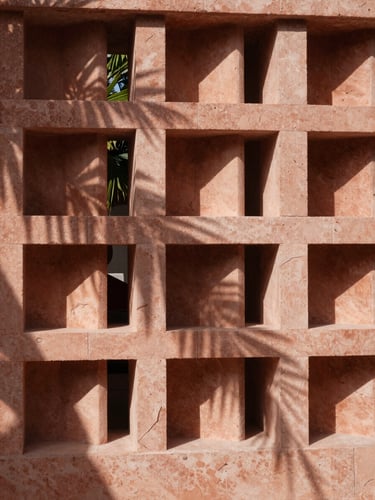 Close-up architectural detail of a modern limestone screen, sculptural light filtering through geometric openings, deep terracotta shadows, high-contrast tropical sun.