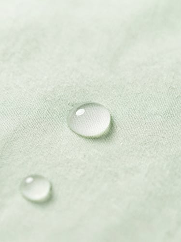 Macro shot of pure water droplets on organic cotton fabric, soft natural morning light, clean sage green tones, portrait aspect