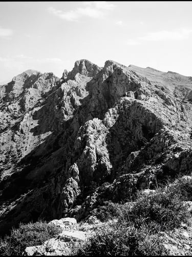 Stark documentary portrait of a rugged limestone mountain ridge in Arcadia, harsh midday sun casting deep black shadows, uncropped 35mm film grain.