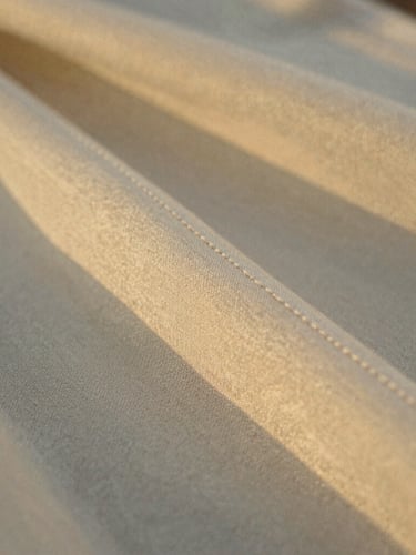Extreme close-up of a hand-stitched silk hem in warm golden hour light, focusing on the refined texture of heritage-mill fabric, shallow depth of field, 35mm film style.