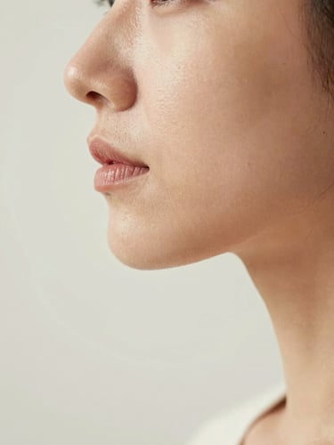 Close-up profile view of a female jaw and neck line from the side, soft diffused north-facing daylight, clinical off-white background, no smile, no full face — the image documents facial contour anatomy as a technical reference, no artifice
