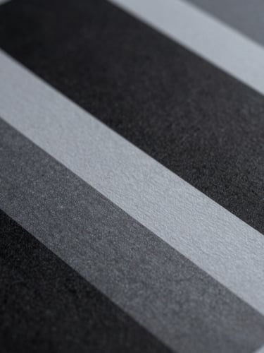 Macro close-up of high-contrast printed brand collateral, deep architectural shadows cast across textured paper grain, cool indirect daylight, minimalist composition.