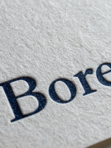 Extreme close-up of heavy cotton paper brand collateral showing rich tactile grain and deep debossed typography, cool lighting.