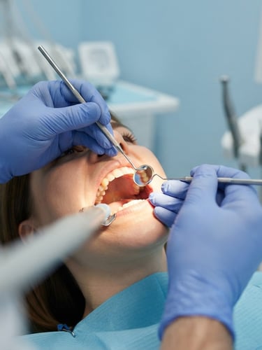 Close-up of a dentist's gloved hands gently examining a patient's mouth under bright clinical lights, sterile tools visible, clean modern operatory background.