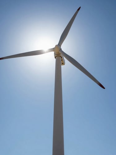 Low-angle technical shot of a single modern wind turbine tower rising into a bright blue desert sky, sharp steel details, sun flare reflecting off the rotor hub.