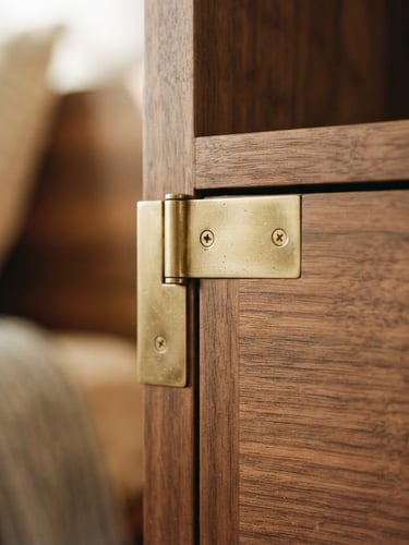 Close-up of hand-finished brass joints on a solid walnut cabinet, warm morning light casting soft shadows, shallow depth of field, 35mm