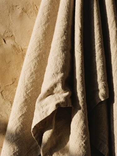 Close-up of structured heavy organic cotton fabric drape, warm afternoon sunlight casting deep shadows on a raw plaster wall, muted earth tones, 35mm photography
