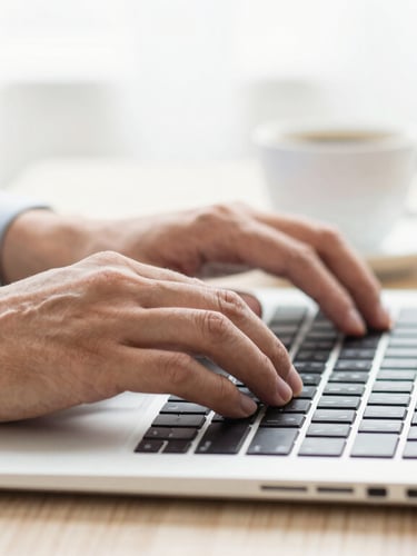 Close-up of a professional's hands typing on a modern laptop next to a cup of coffee, bright natural daylight, clean workspace, shallow depth of field