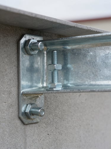 Close-up documentary shot of a galvanized steel canopy bracket bolted into a concrete wall, hex bolts and washer plates clearly visible, natural overcast daylight from the side, sharp depth of field on the fastener detail