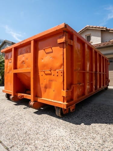 Low-angle wide shot of a clean, heavy-duty orange steel roll-off dumpster parked on a residential driveway in bright California daylight, sharp shadows, industrial textures