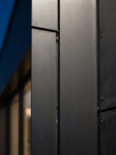 Extreme close-up of a dark grey aluminum composite panel joint, clean architectural line, raw steel texture, sharp daylight lighting, professional exterior photography.