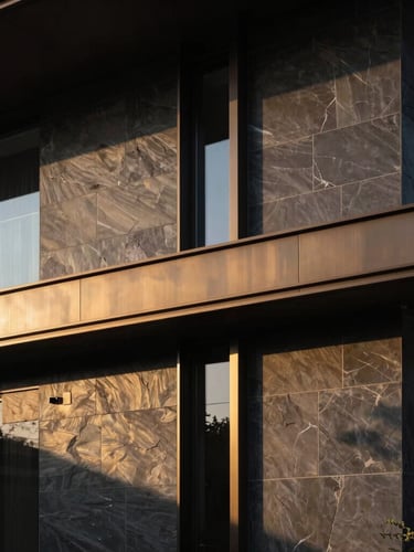 Low-key dramatic architectural detail of a modern luxury home exterior, dark slate and brushed bronze facade, sharp golden hour shadows, minimal composition.