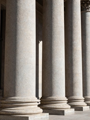 Sharp architectural detail of an institutional building in Madrid, clean granite columns, high-contrast natural daylight with deep shadows.
