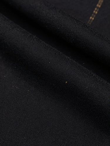 Macro close-up of heavy-drape black cotton fabric texture, showing precise embossed detailing and raw textile fibers, high-contrast studio lighting, desaturated tones