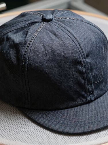High-contrast workshop side-light illuminating a structured Richardson cap secured in an industrial embroidery hoop, sharp details of mesh backing