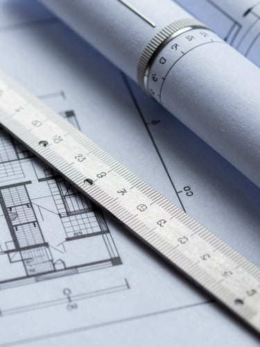 Extreme close-up of architectural blueprints with a steel drafting scale resting on the paper, high-contrast technical daylight, cool slate tones