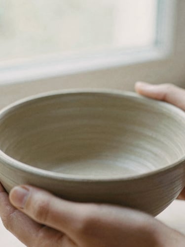 Close-up macro shot of hands holding the unpolished clay rim of a ceramic bowl, soft north-facing window light, 35mm film texture