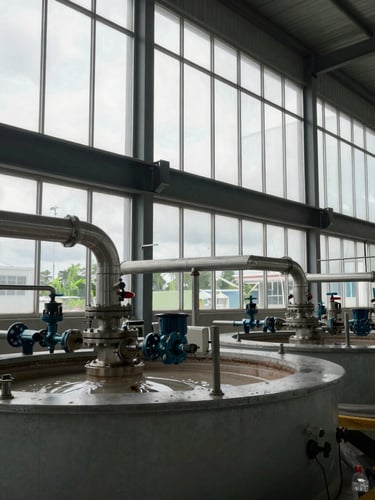 Wide environmental shot of industrial electrolysis machinery inside a newly constructed facility in Pekan, Pahang, overcast daylight filtering through high windows, steel pipes and technical valves visible.