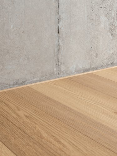 Close-up of pristine custom oak flooring meeting a raw concrete wall with absolute precision, sharp architectural lines