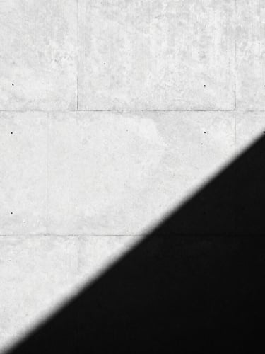 High-contrast black and white architectural photography, dramatic sharp shadows on a concrete wall, minimalist composition, 35mm lens