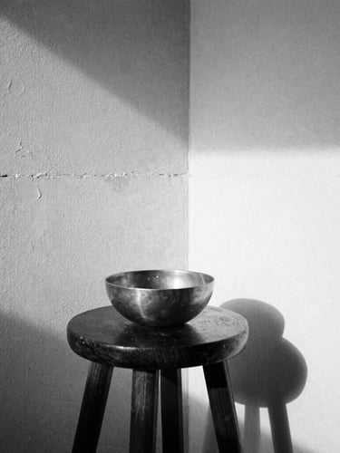 Extreme close-up of a sunlit corner of a minimalist room, raw concrete wall, a single dark wooden stool with a brass bowl, sharp natural shadows, monochrome, 35mm