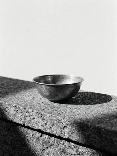 Minimalist monochrome photography of a single brass bowl on a raw stone ledge, stark natural light from the side, deep black shadows, 35mm