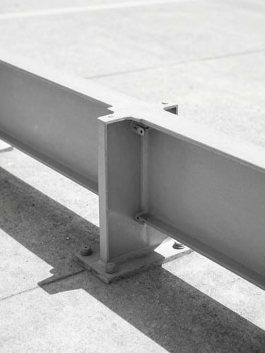 A portrait orientation shot of a structural steel I-beam joint with heavy industrial bolts, harsh midday sun creating sharp geometric shadows on concrete, minimalist architectural photography, high contrast monochrome tones, sharp focus, 35mm lens