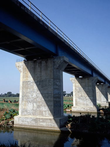 Industrial concrete bridge foundations spanning a rural canal, sharp daylight, structural engineering focus, blue sky